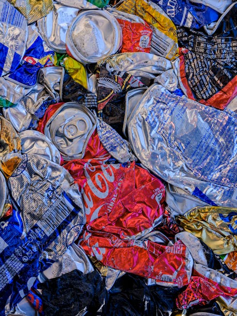 A close-up view of multiple black plastic rubbish bags filled with waste, tightly tied at the top, resting against a plain, light-colored wall. The bags have a shiny, crinkled texture and are placed o