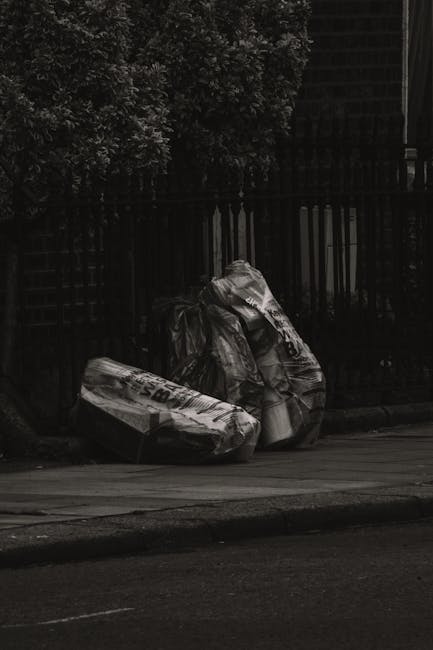 A narrow urban alleyway with uneven, muddy ground and scattered debris. On the right side, there are large white items, likely domestic appliances such as a washing machine and possibly other discarde